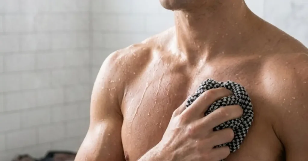 Homme se frottant le torse sous la douche avec une serviette exfoliante après le sport